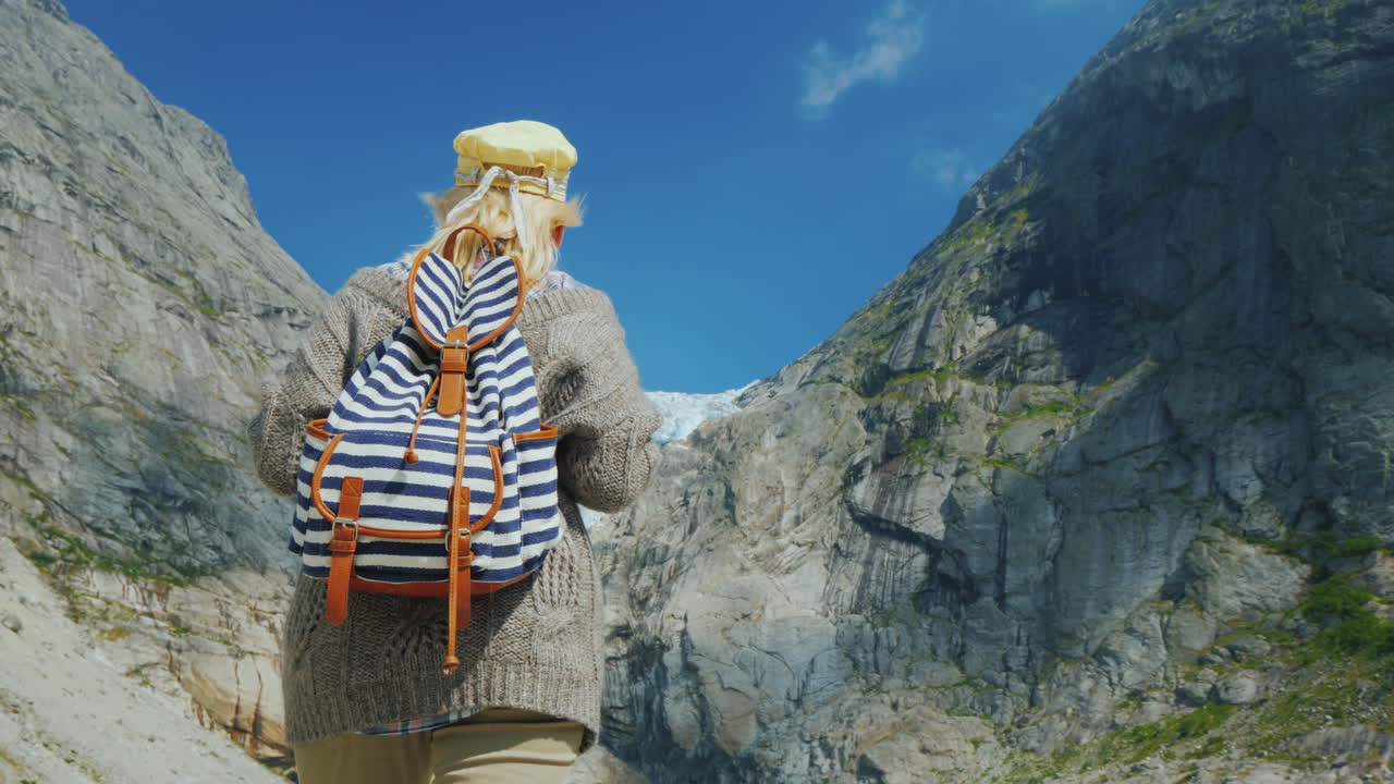 una mujer con ropa abrigada admira el glaciar en lo alto de las montañas glaciar briksdal en noruega un viaje