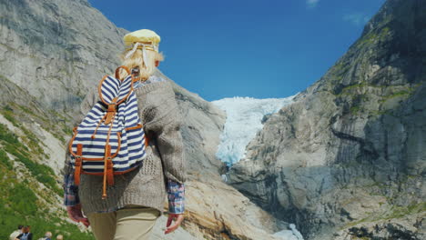 A-Woman-In-Warm-Clothes-Admires-The-Glacier-High-In-The-Mountains-Briksdal-Glacier-In-Norway-A-Trip-
