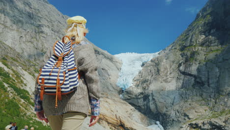 a woman in warm clothes admires the glacier high in the mountains briksdal glacier in norway a trip