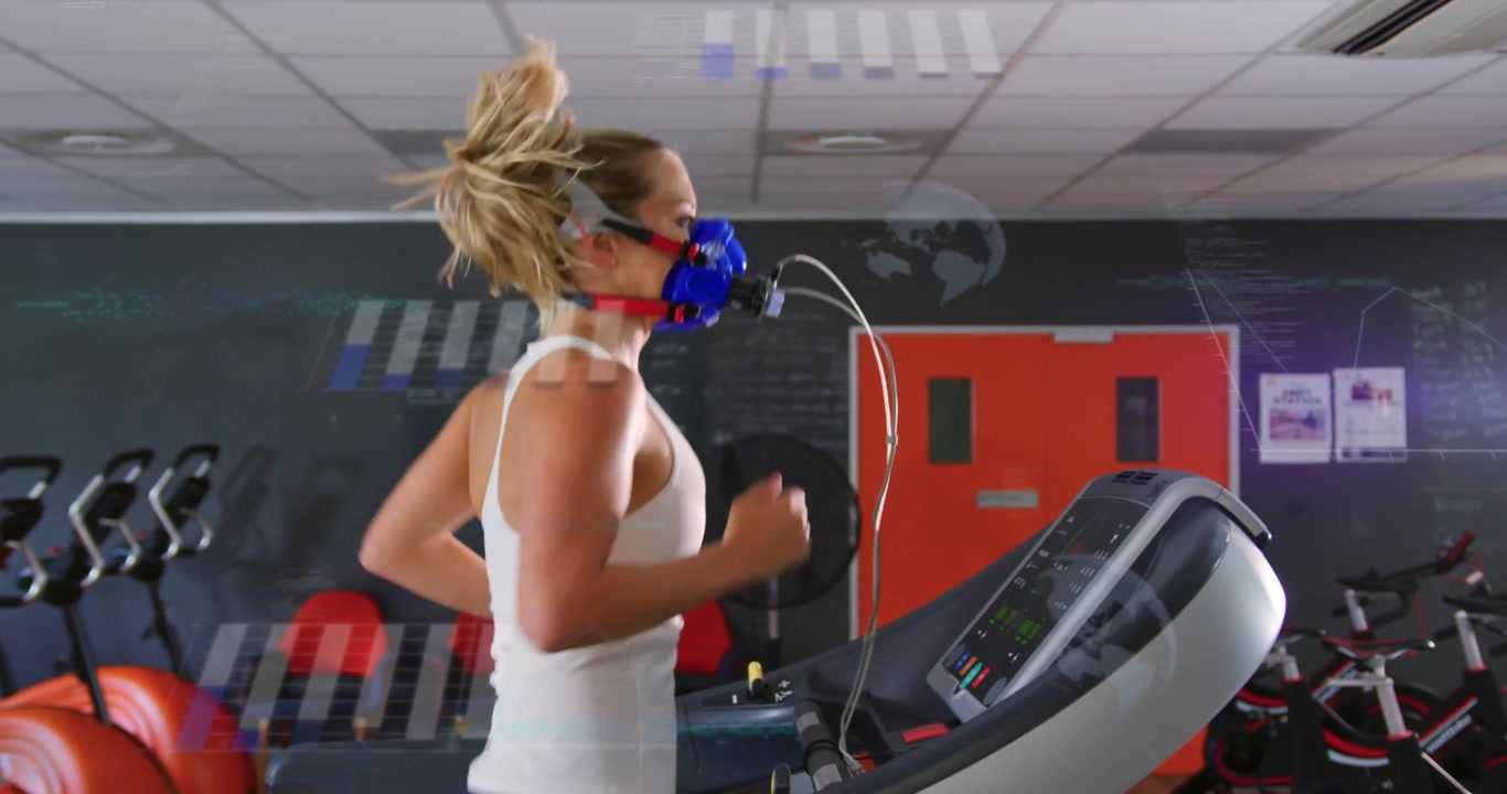 Monitor che si avvia, donna di mezza età che corre sul tapis roulant in palestra per dei test, indossando una canotta bianca e una maschera blu.