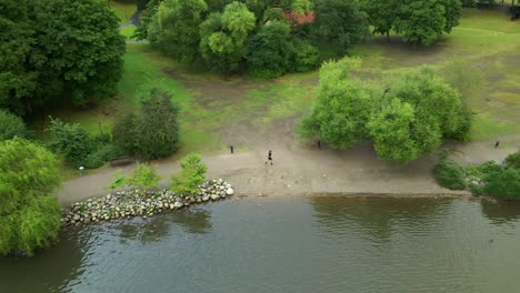 a female running a long sida of a small lake with trees and grass in the background