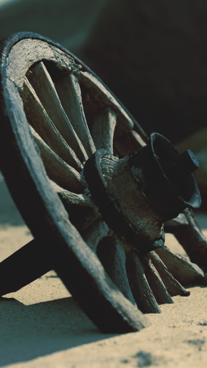 Rustic wooden wheel rests on sandy ground under sunlight near rocky area
