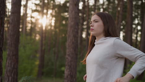 female rotates shoulders doing exercise at sunset. young woman performs warm-up activity preparing for fitness workout standing in evening forest