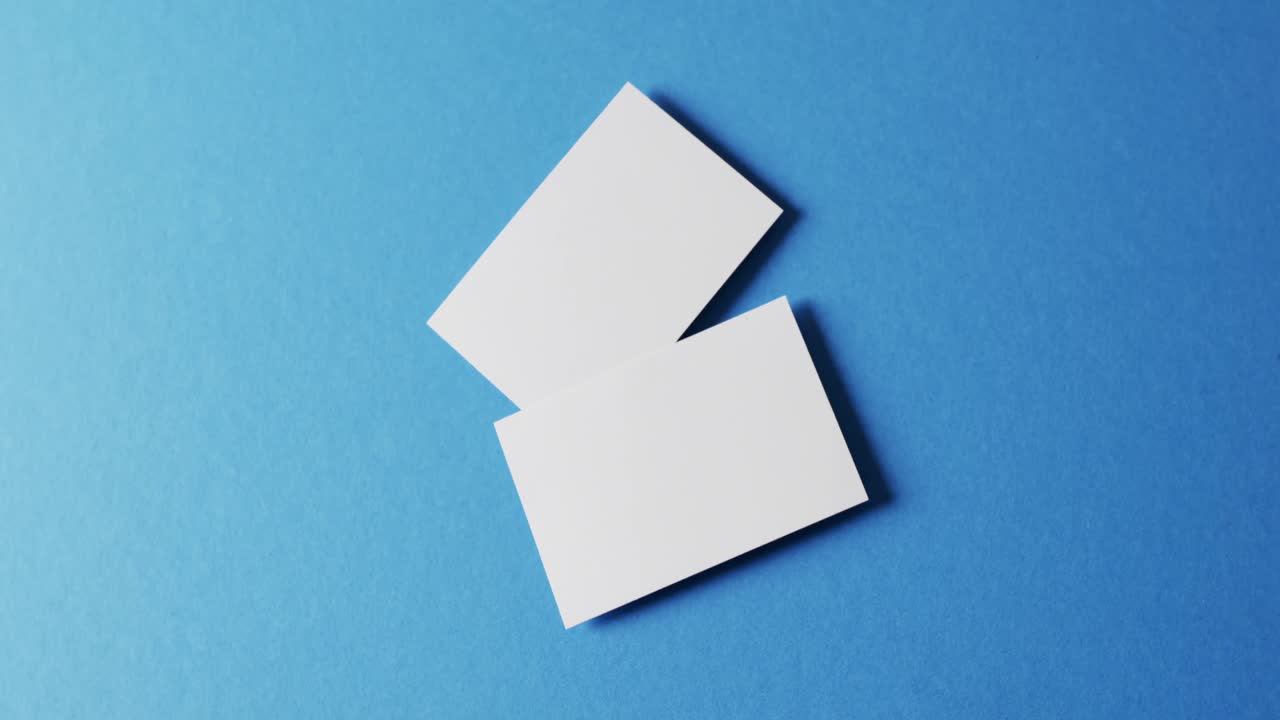 vista aérea de tarjetas de visita blancas y blancas sobre fondo azul, espacio de copia, cámara lenta