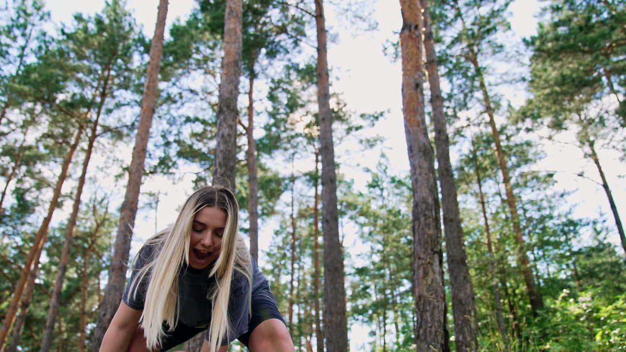 Blonde long-haired woman entertaining her baby in nature. Smiling mom waving her child back and forth. Low angle view.