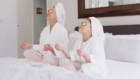 Video-of-happy-asian-mother-and-daughter-in-robes-doing-cucumber-mask-and-resting