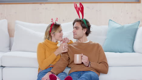 couple wearing festive headbands enjoying hot drinks at home during christmas