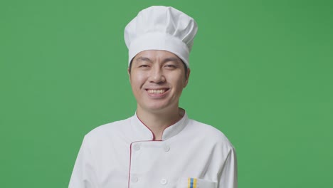 primer plano del chef asiático de pie y sonriendo a la cámara en el estudio de fondo de la pantalla verde