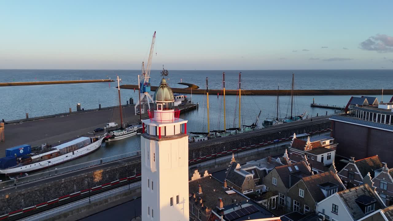 Ren cirkulær droneflyvning omkring fyrtårnet, der afslører hustage, både og havet.