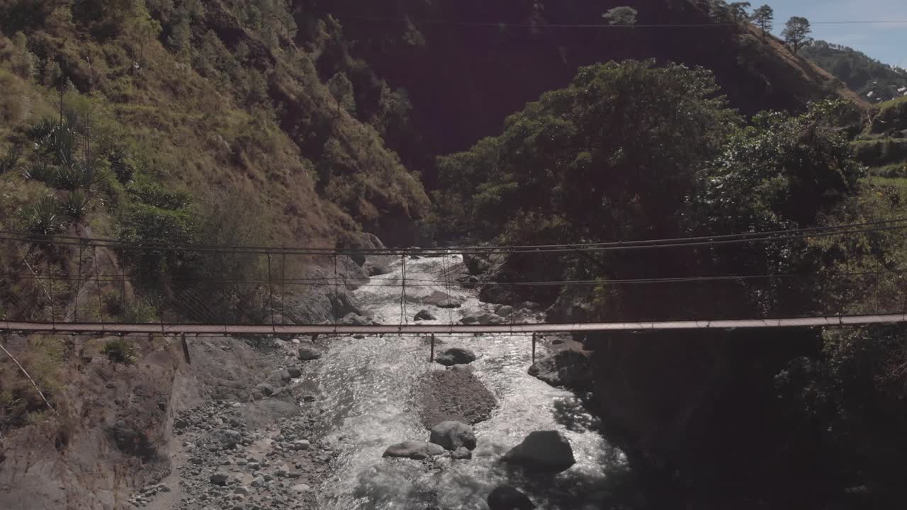 puente colgante de alambre de metal que se extiende sobre el río en un terreno remoto y salvaje antena estacionaria de gran angular medio