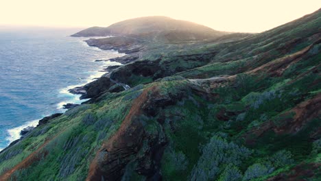 Drohne,-Die-Während-Des-Sonnenuntergangs-Durch-Berghügel-über-Einer-Hawaiianischen-Küstenstraße-Fliegt