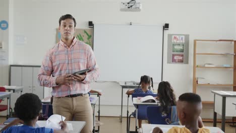 diverse children at desks and male teacher using tablet in elementary school class, slow motion