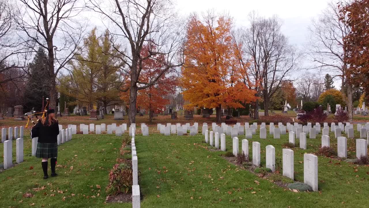 A red-haired bagpiper walks down a row of graves at a cemetery