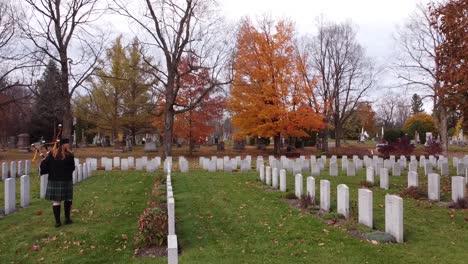a red-haired bagpiper walks down a row of graves at a cemetery