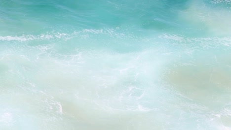 close-up view of turquoise ocean waves swirling and creating white foam patterns.