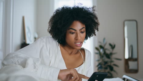 relaxed girl browsing cell phone bedroom. curly positive lady laying hotel bed