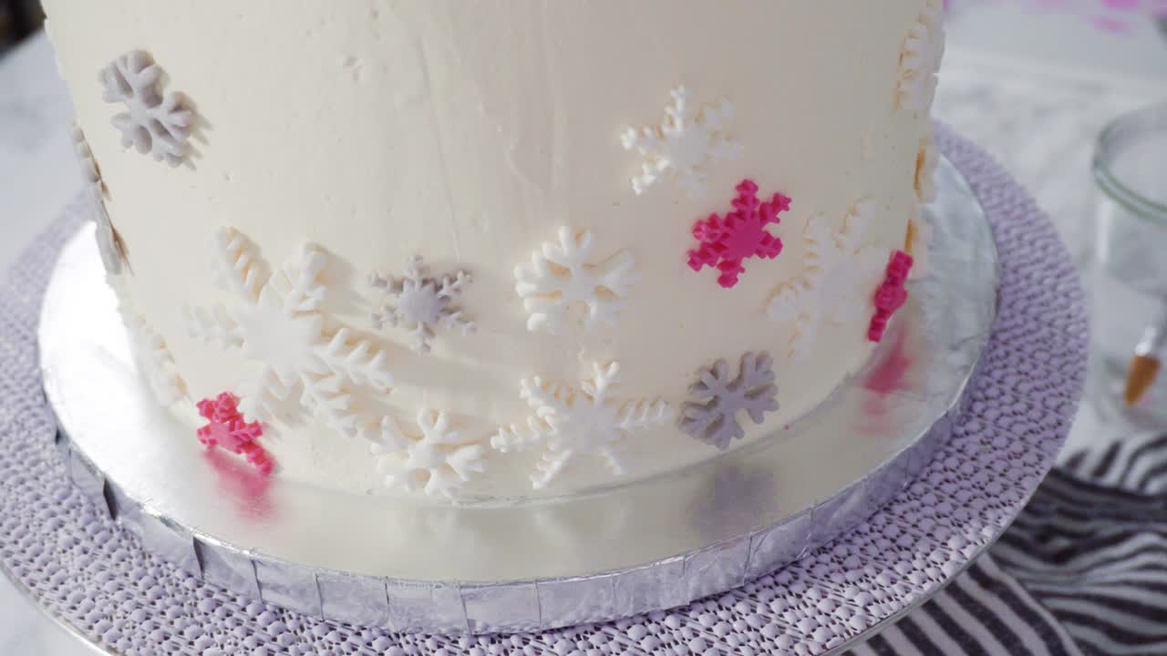 Decorating round funfetti cake with pink and white fondant snowflakes.
