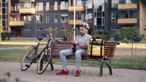 food delivery guy seated on a bench having a cup of tea during his break