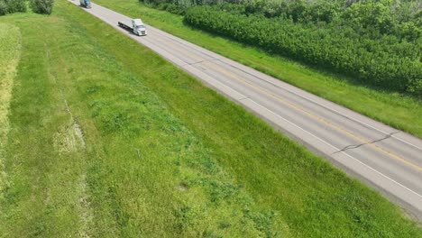 a couple semi trucks heading down a 2 lane blacktop highway on a sunny summer day