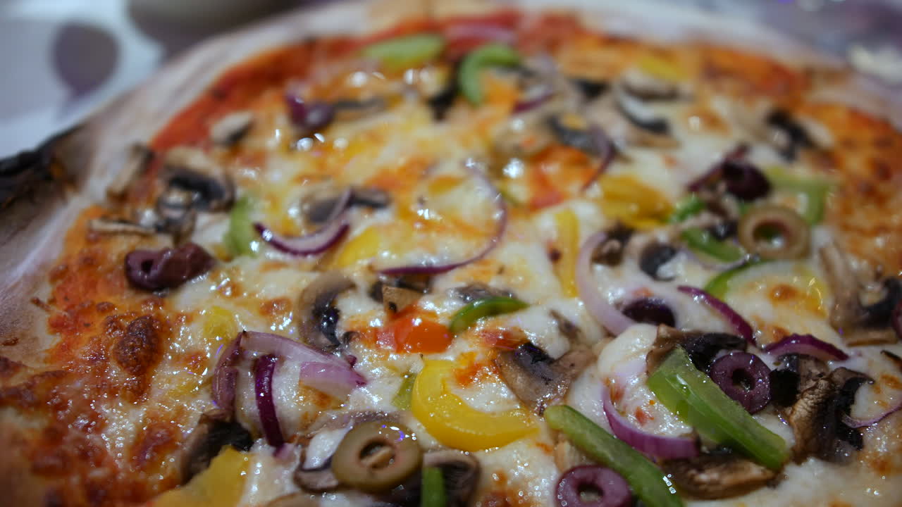 A freshly baked vegetable pizza topped with mushrooms, bell peppers, red onions, and olives sits on a plate. The crispy, golden crust and melted cheese are paired with colorful, fresh toppings