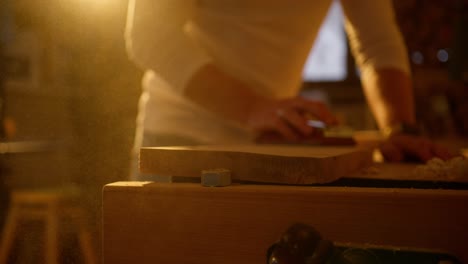 Scenic-close-up-of-man-filing-wood-in-a-workshop-with-sunset-light-behind