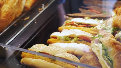 el asistente de la tienda, usando pinzas de metal, toma el sándwich de pollo de la exhibición de una tienda local