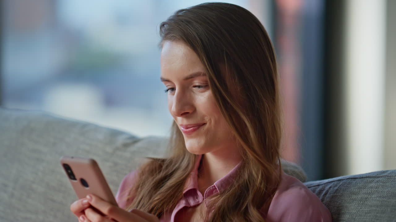 Joyful woman texting phone sitting on couch home closeup. Smiling brunette