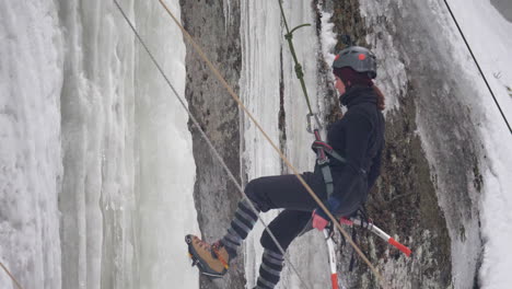 A-woman-with-axes-and-crampons-repelling-down-a-huge-frozen-rock-face