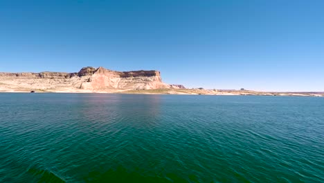 Una-Casa-Flotante-Navega-Por-Las-Aguas-Turquesas-Del-Lago-Powell,-Page,-Arizona,-Pasando-Por-Las-Colinas-De-Arenisca-Que-Bordean-La-Orilla-Del-Lago