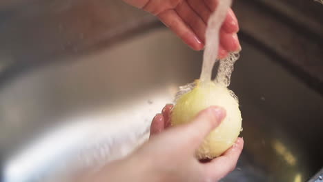 female hands washing a white onion in the kitchen sink in slow motion