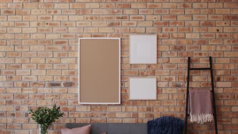 Three-wooden-frames,-plant-and-sofa-with-copy-space-on-brick-wall