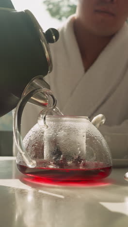 hombre vierte agua de la tetera en la tetera. té de frutas elaborado llenando gradualmente con agua con la ayuda de un joven. mesa de comedor con bebida caliente