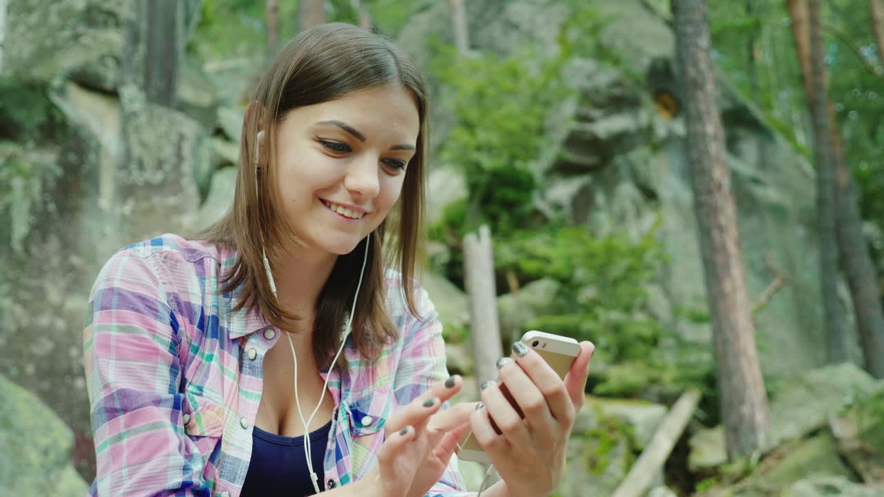 una joven turista usa un teléfono inteligente en una caminata sentada descansando contra las rocas en las montañas 4k