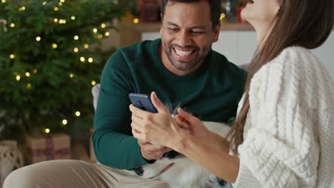 Glückliches-Paar-Mit-Mehreren-Ethnien,-Das-Zu-Weihnachten-Zu-Hause-Ein-Foto-Mit-Hund-Macht.