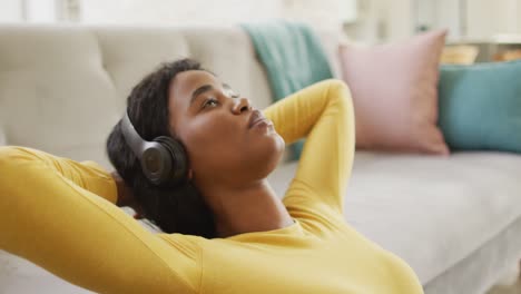 Video-Einer-Entspannten-Afroamerikanischen-Frau,-Die-Kopfhörer-Trägt-Und-Auf-Dem-Boden-Sitzt