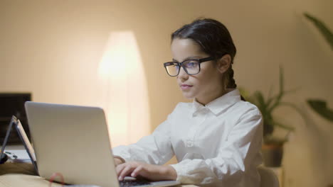 Smart-schoolgirl-working-on-laptop-in-the-evening-at-home