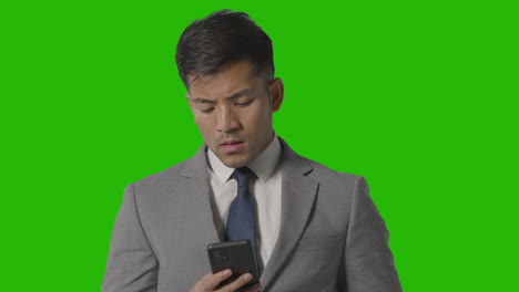 Foto-De-Estudio-De-Un-Hombre-De-Negocios-Frustrado-En-Traje-Contra-La-Pantalla-Verde-Mirando-El-Teléfono-Móvil