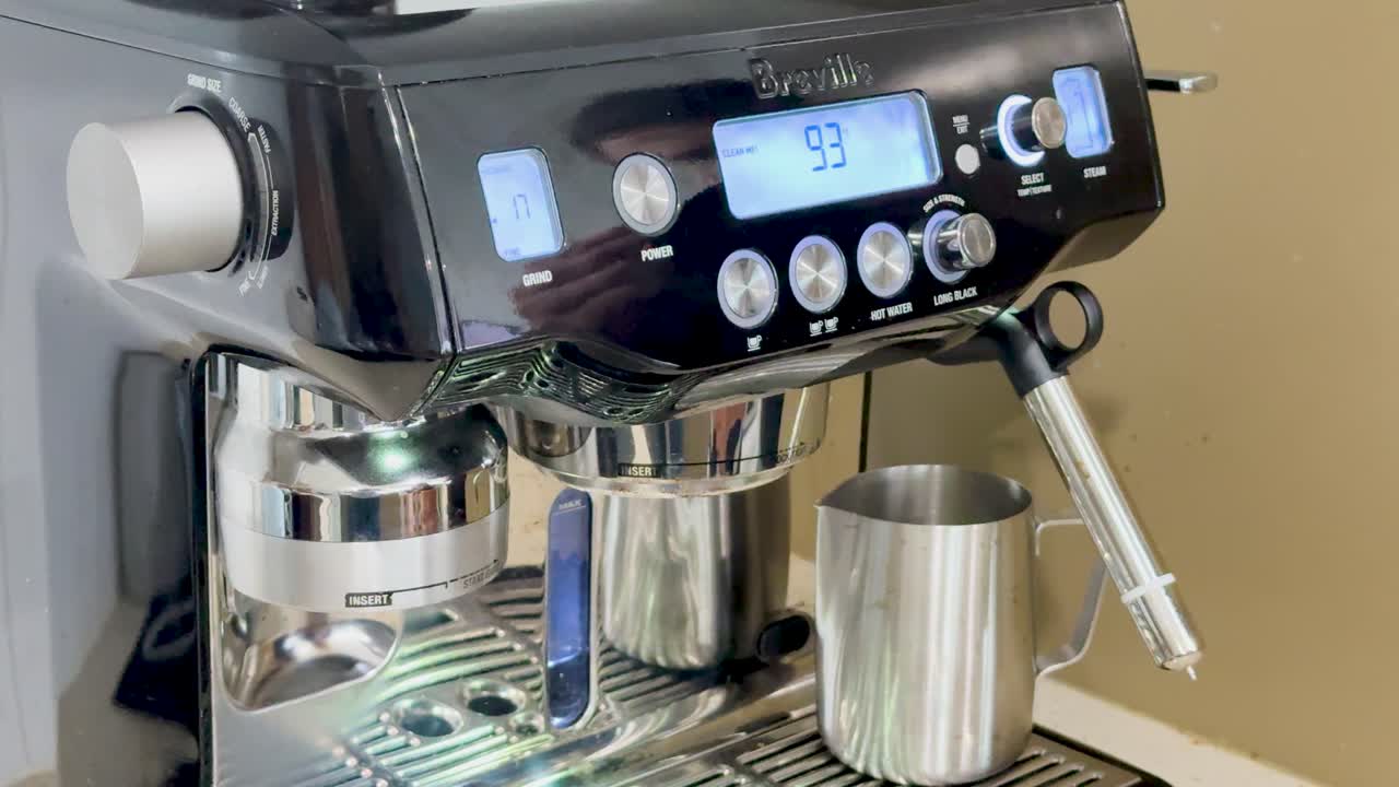 A person interacts with a digital espresso machine, adjusting settings and preparing for coffee brewing in a well-lit kitchen