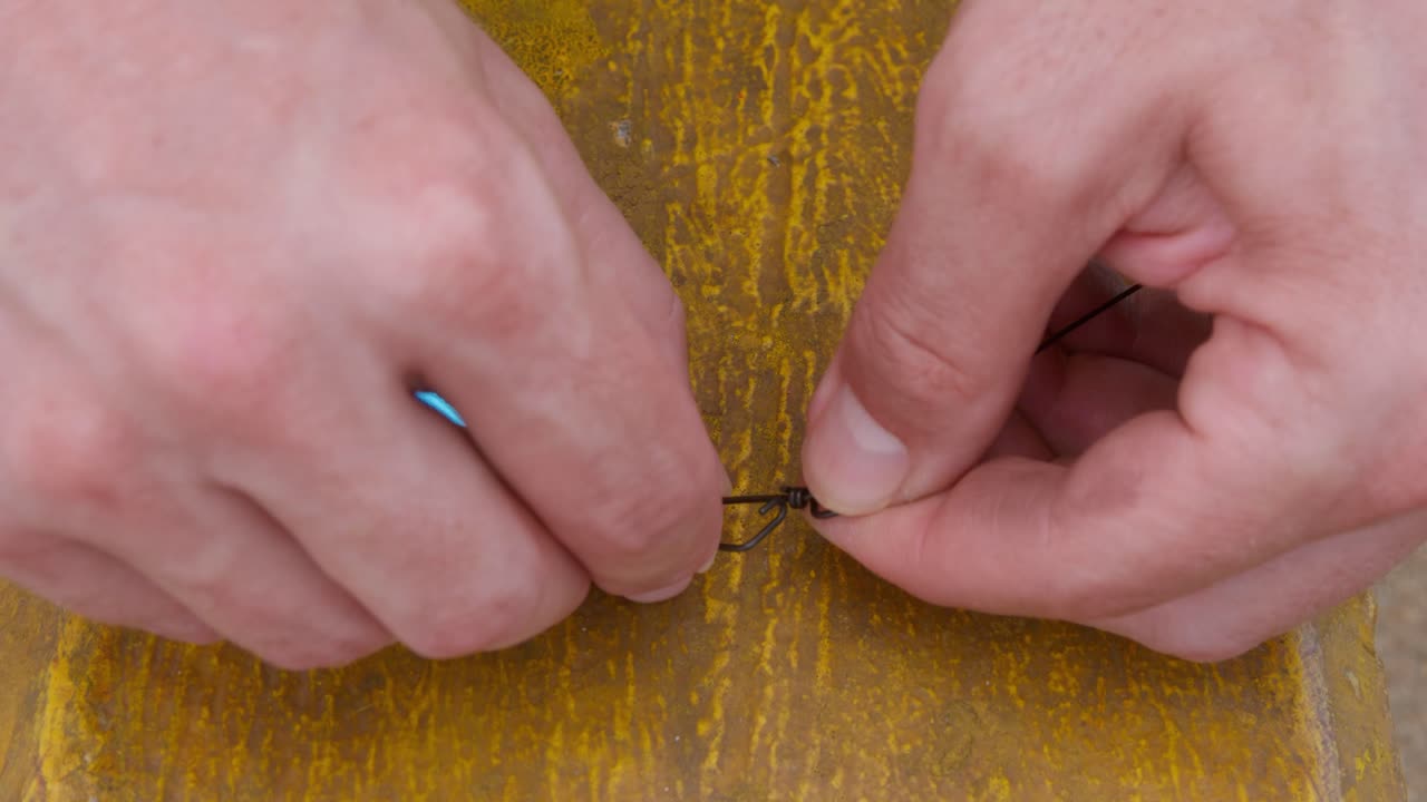 Man from outback Australia fishing from a remote pier on an overcast, wet season day. Attaching a metal lure to trace. In slow motion, clip 1