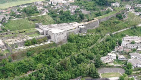 Drone-view-in-Albania-flying-in-Gjirokaster-town-over-a-medieval-castle-on-high-ground-fort-showing-the-brick-brown-roof-houses