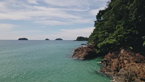 aerial dolly shot of tropical rocky coastline and four tropical islands in the background