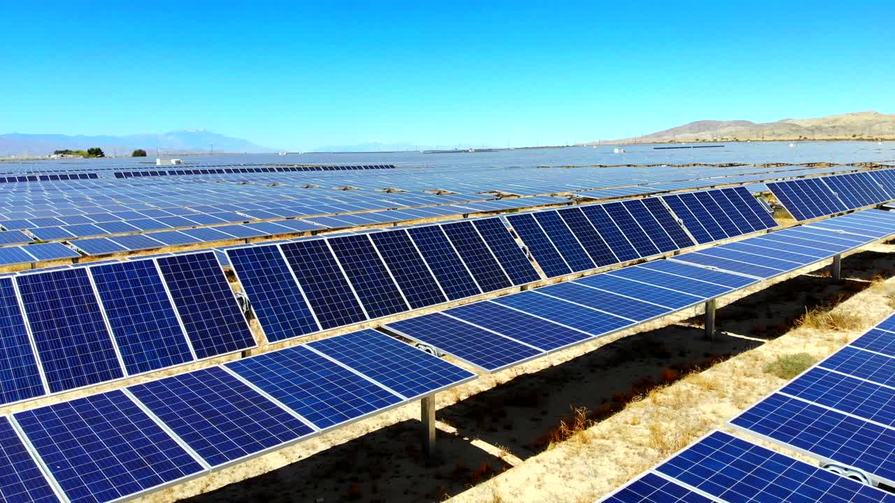 Lateral aerial drone sweep and pan over huge solar photovoltaic panel power generating farm in desert with reflecting sun, 4k