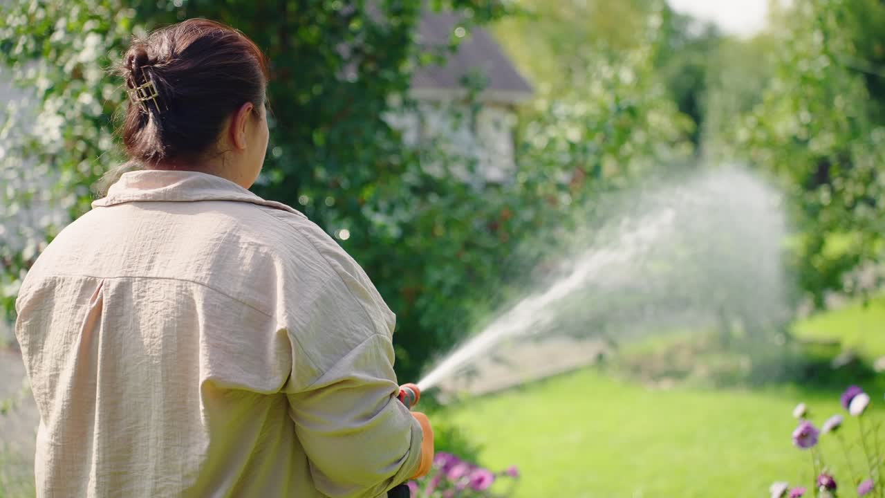 Gioia nel giardinaggio: una donna innaffia il suo rigoglioso giardino con un tubo, godendosi la bellezza della natura tra fiori vivaci in una giornata di sole