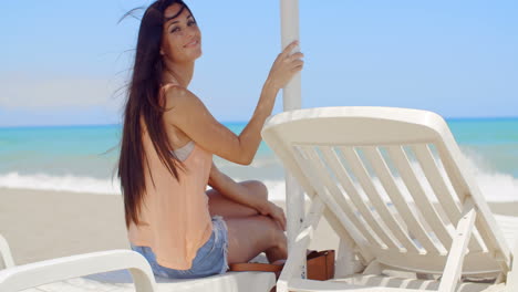 Lächelnde-Hübsche-Frau-Sitzt-Auf-Einer-Sonnenliege-Am-Strand