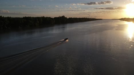 ascending aerial shot of speedboat cruising towards sunset on amazon river