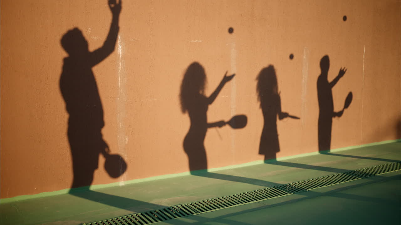 The shadow of two men and two women practicing to play pickleball on a court on a sunny day