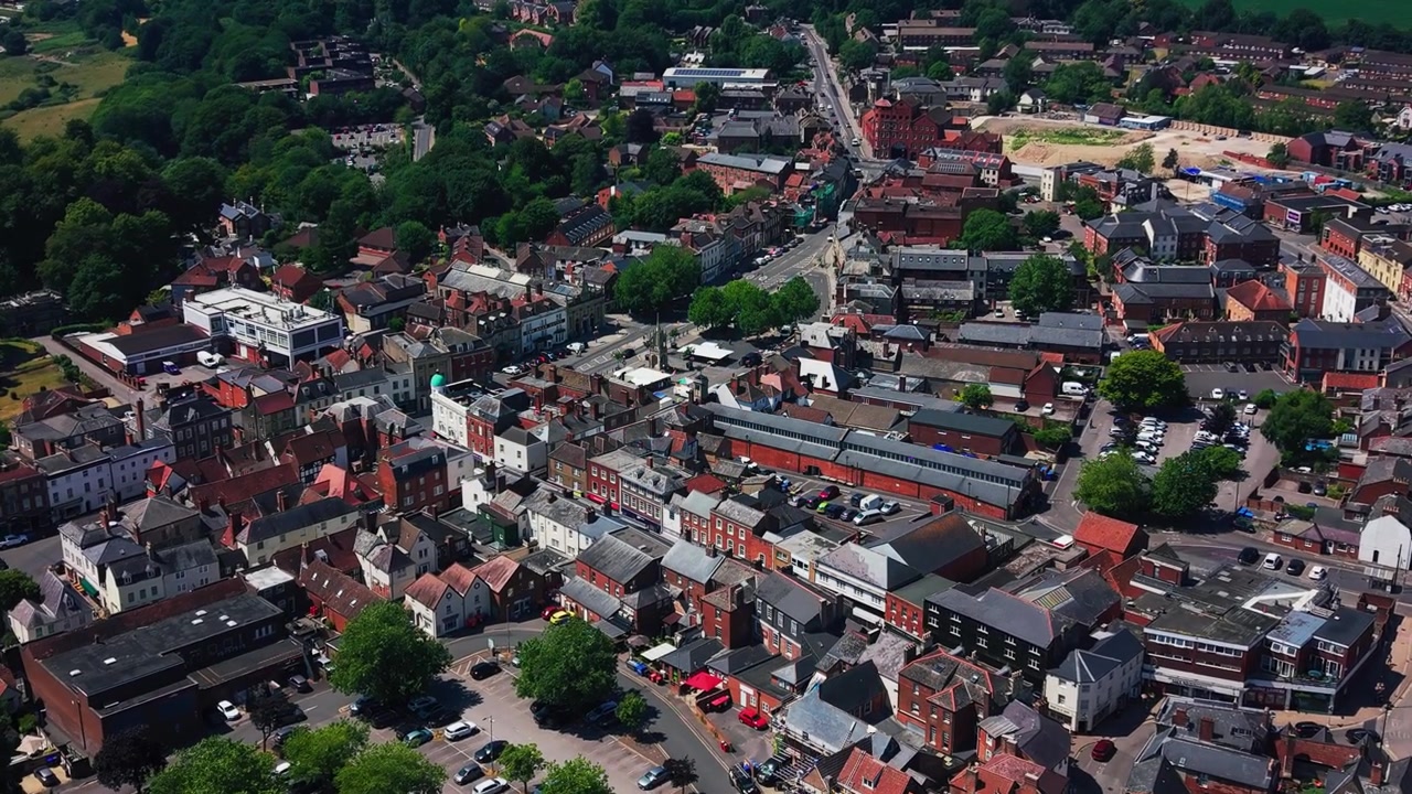 Høj droneudsigt over det centrale Devizes i Wiltshire, der viser historiske hustage, butikker, veje, parkeringspladser, beboelsesgader og landbrugsland i det fjerne på en solrig sommerdag