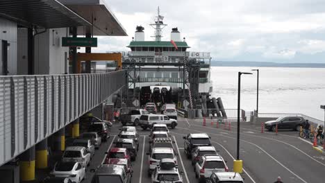 vehicles line up and drive onto a ferry at colman dock in seattle, preparing for a maritime journey across puget sound on a cloudy day.