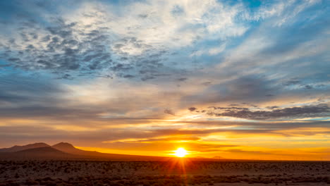 a golden sunrise illuminates the mojave desert landscape at dawn with a colorful cloudscape overhead - wide angle time lapse