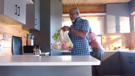happy senior african american couple unpacking groceries in kitchen, slow motion